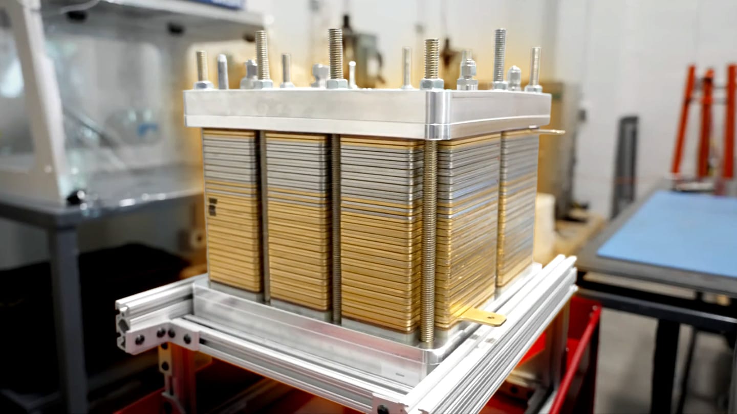 Industrial stack of metal plates held together by bolts, likely a heat exchanger core in a lab or workshop setting.