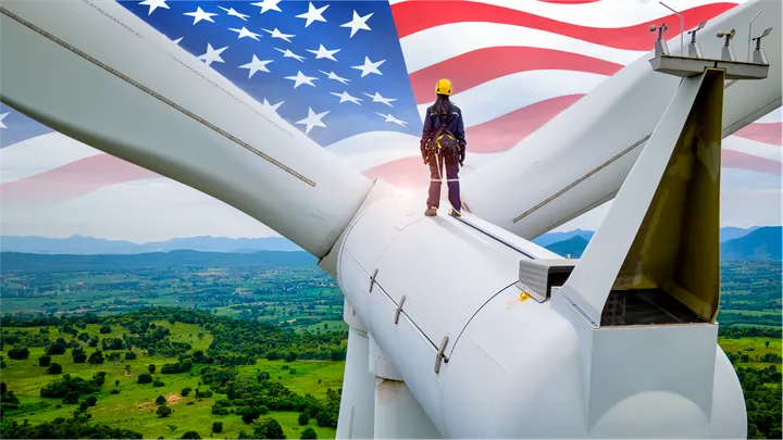 A figure stood atop a wind turbine, looking over a wooded area, with the American flag imposed over the sky