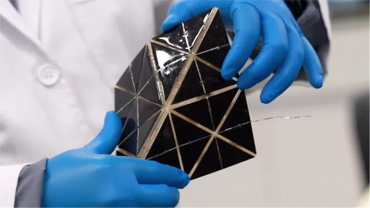 A pair of blue-gloved hands holding a 3d shifting solar panel