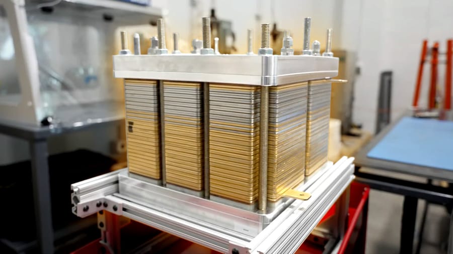 Industrial stack of metal plates held together by bolts, likely a heat exchanger core in a lab or workshop setting.